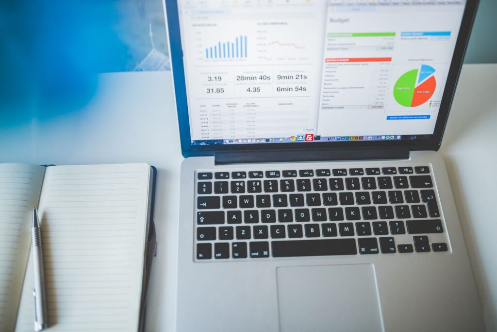 Laptop showing colourful charts beside a notebook and pen